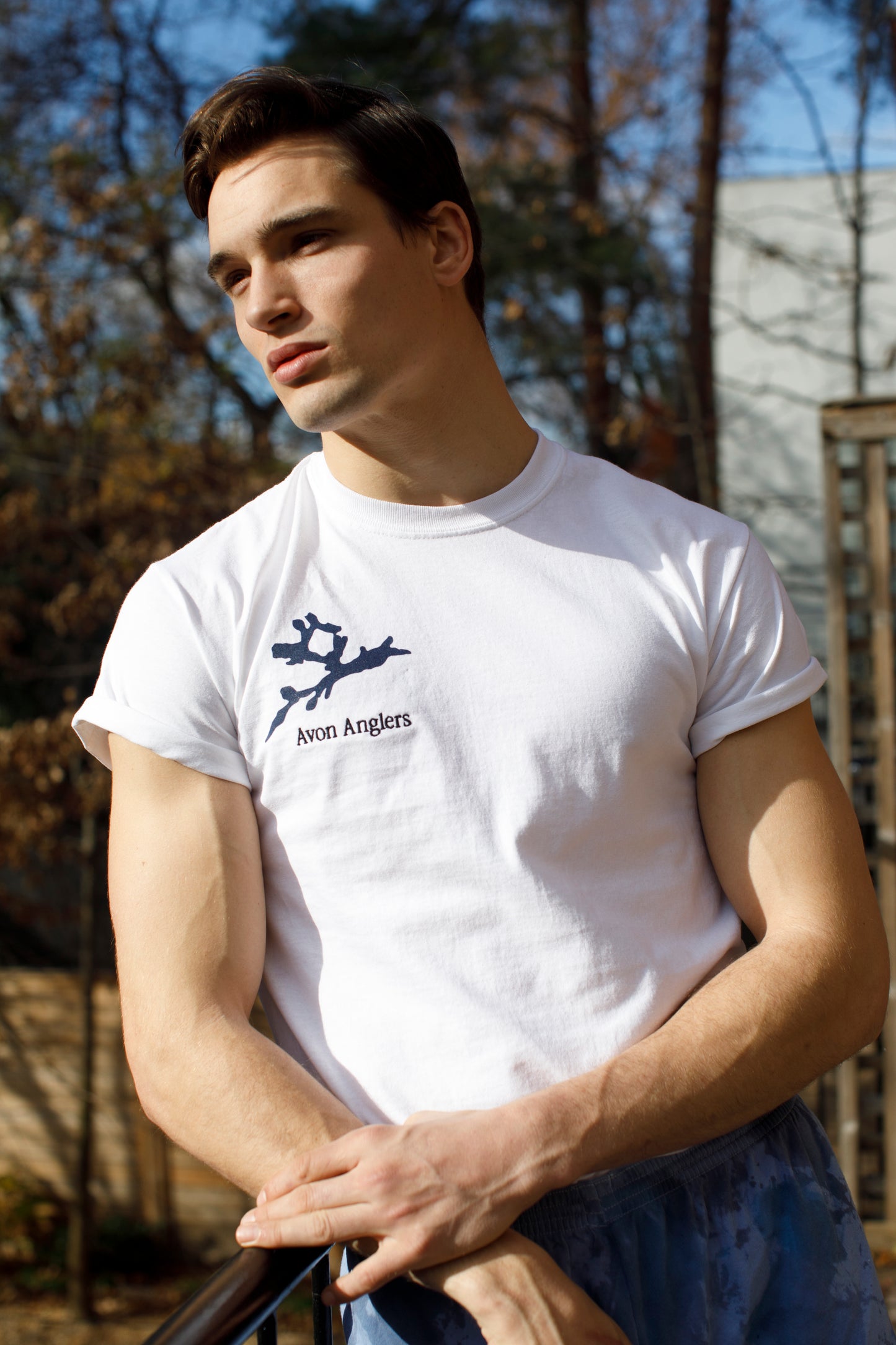 Footballer Mason looks off in the distance wearing the white tshirt with navy blot on the right chest with black logo embroidery