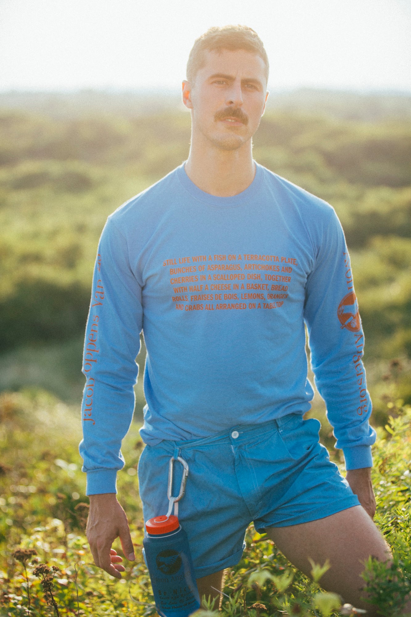 model standing in sand dunes wears a sky blue Jacob Foppens Van Es long sleeve t-shirt